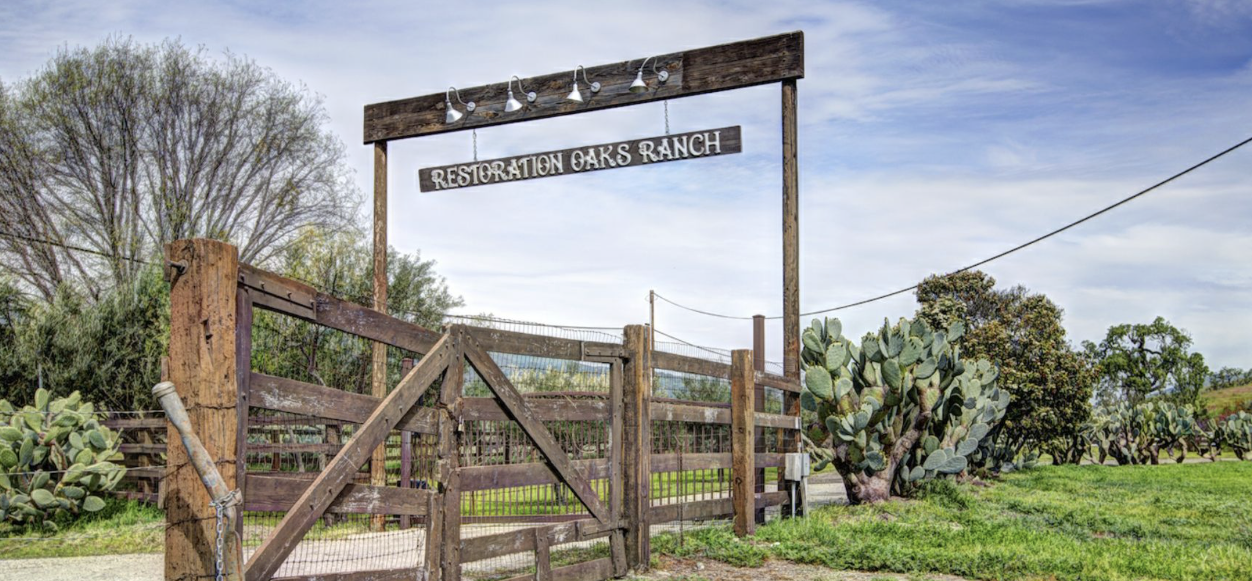 Wooden gate entrance to Restoration Oaks Ranch with trees and blue sky in the background